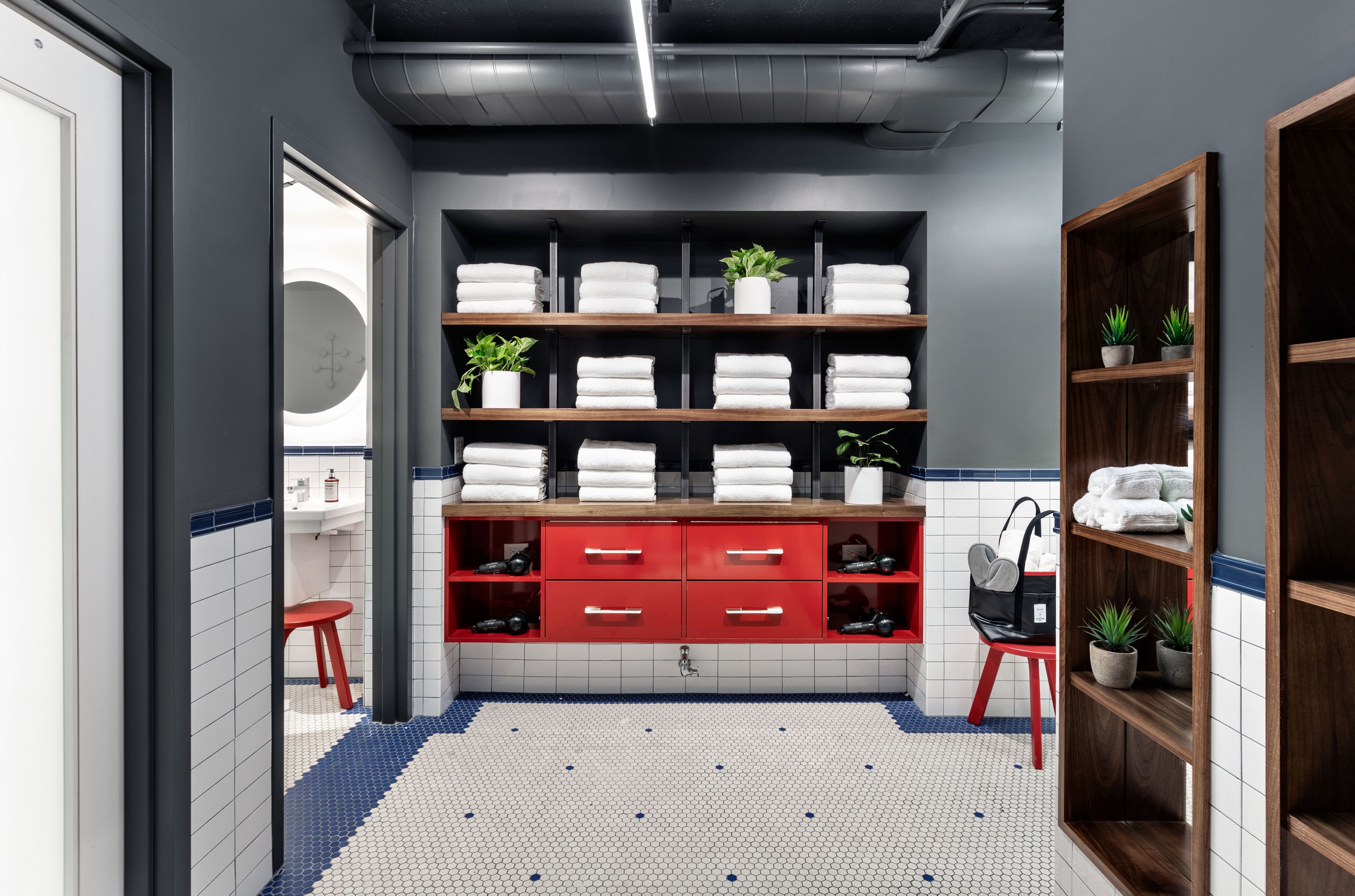 A modern bathroom with a tiled floor, a red vanity with drawers, and shelves with towels and plants.