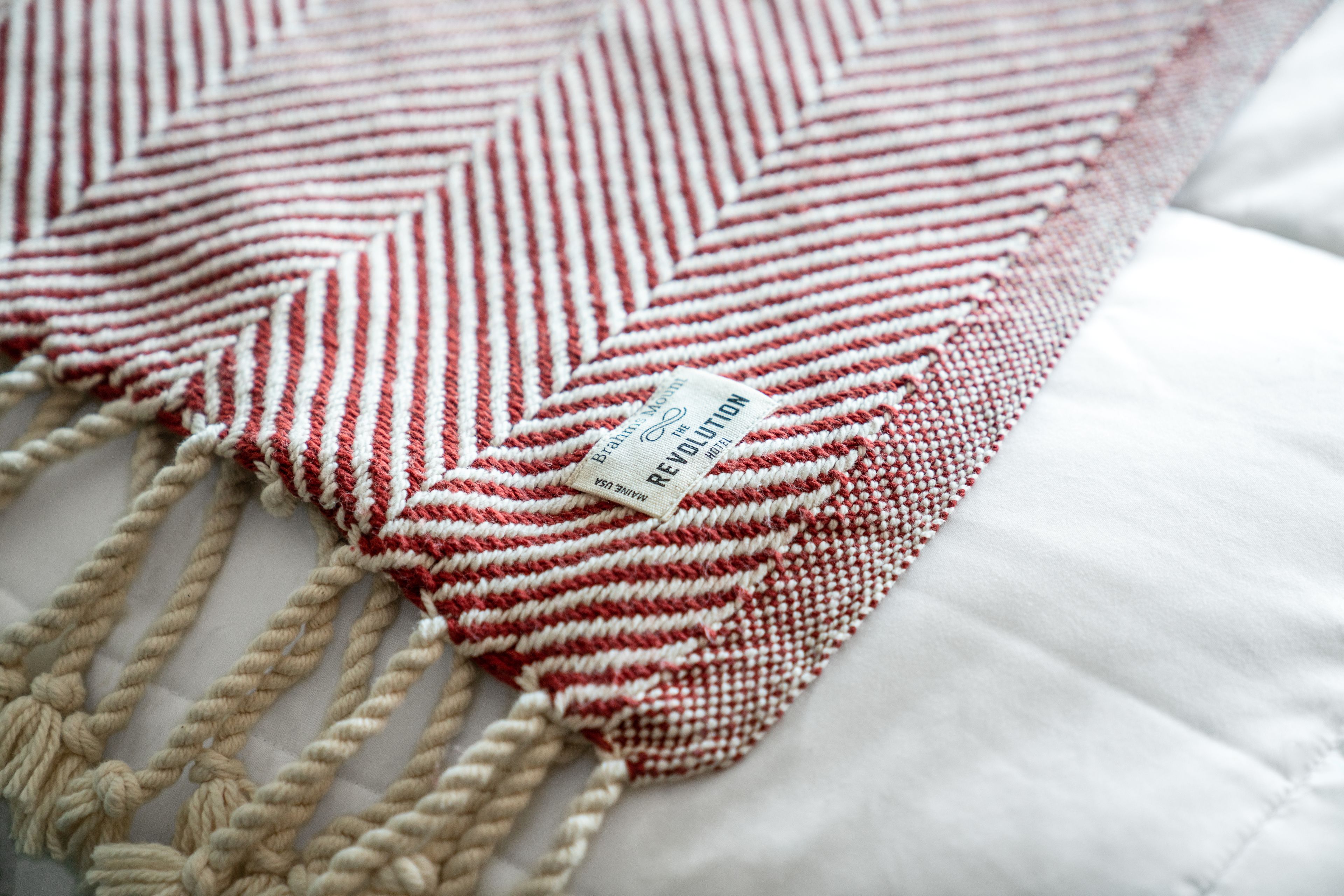 A close-up of a red and white striped macrame pillow with a tag.
