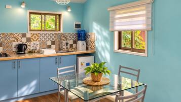 A modern kitchen with blue cabinets, a glass dining table, and a coffee maker.
