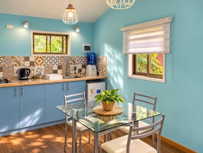 A modern kitchen with blue cabinets, a glass dining table, and a coffee maker. - Cabañas Raupa (Hanga Roa)