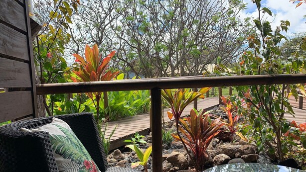 A wicker chair with a cushion and a glass table on a wooden deck. - Cabañas Raupa (Hanga Roa)