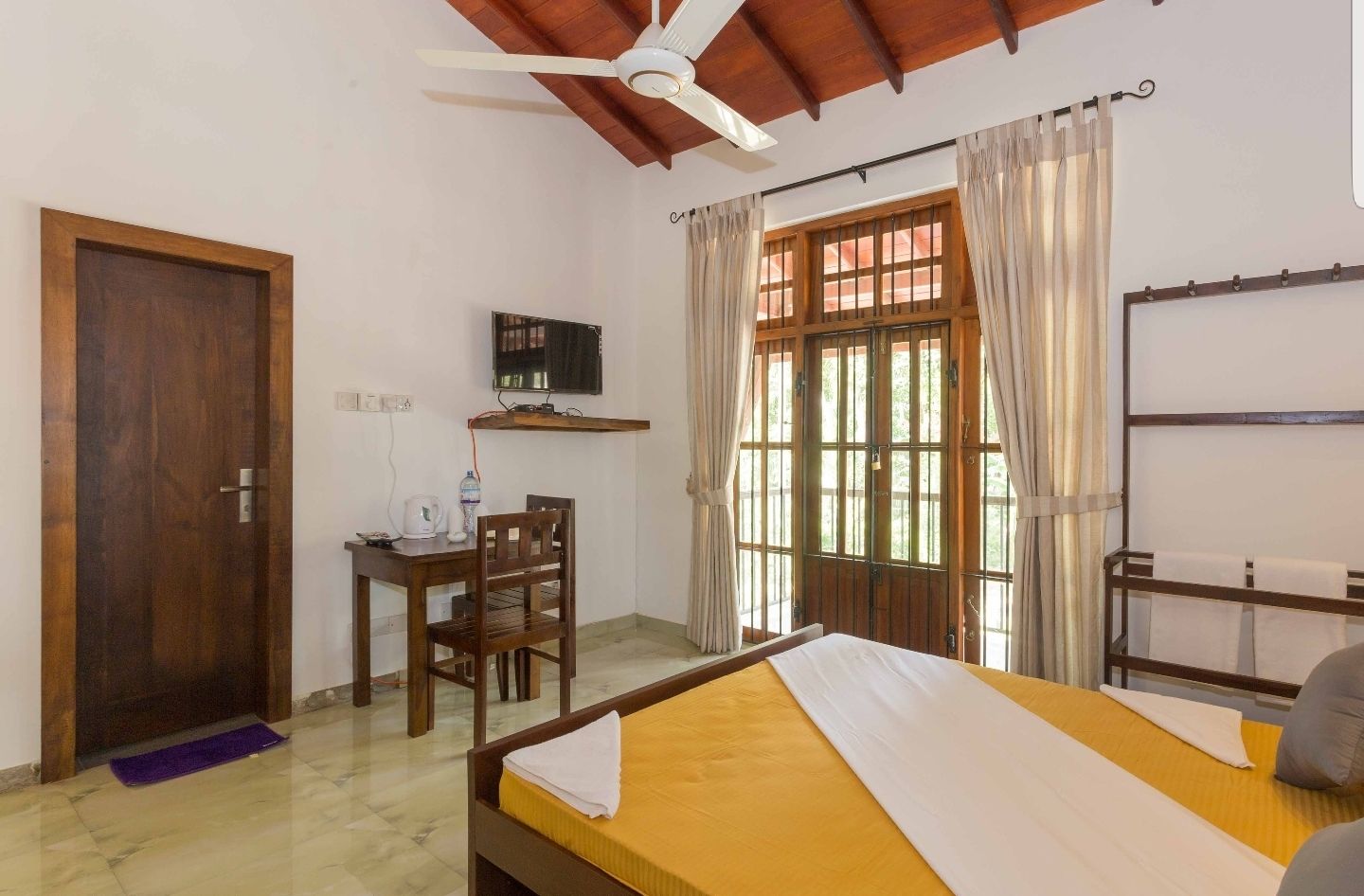 Una habitación con cama, escritorio, silla, televisor y ventana con cortinas.