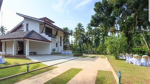 A large, modern building with a covered patio area and a paved walkway leading to a seating area with white chairs and gold sashes. - Araliya Cottage (Negombo)