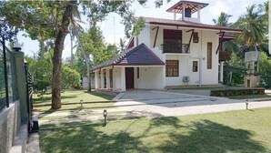 A two-story house with a tiled roof, a front porch, and a well-maintained lawn. - Araliya Cottage (Negombo)