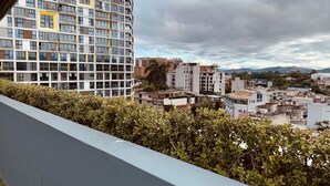 Ein Hochhaus mit einer rasterförmigen Fassade, umgeben von dichter Vegetation und weiteren Gebäuden.