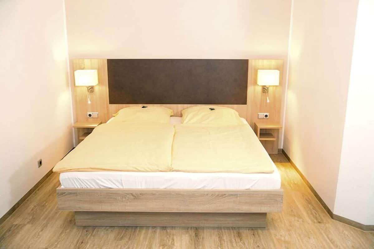 Un lit double avec un cadre en bois, deux tables de chevet avec des lampes et une tête de lit.