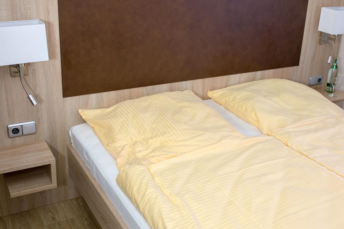 Un lit double avec une tête de lit en bois et deux tables de chevet, chacune équipée d’une lampe et d’une bouteille.