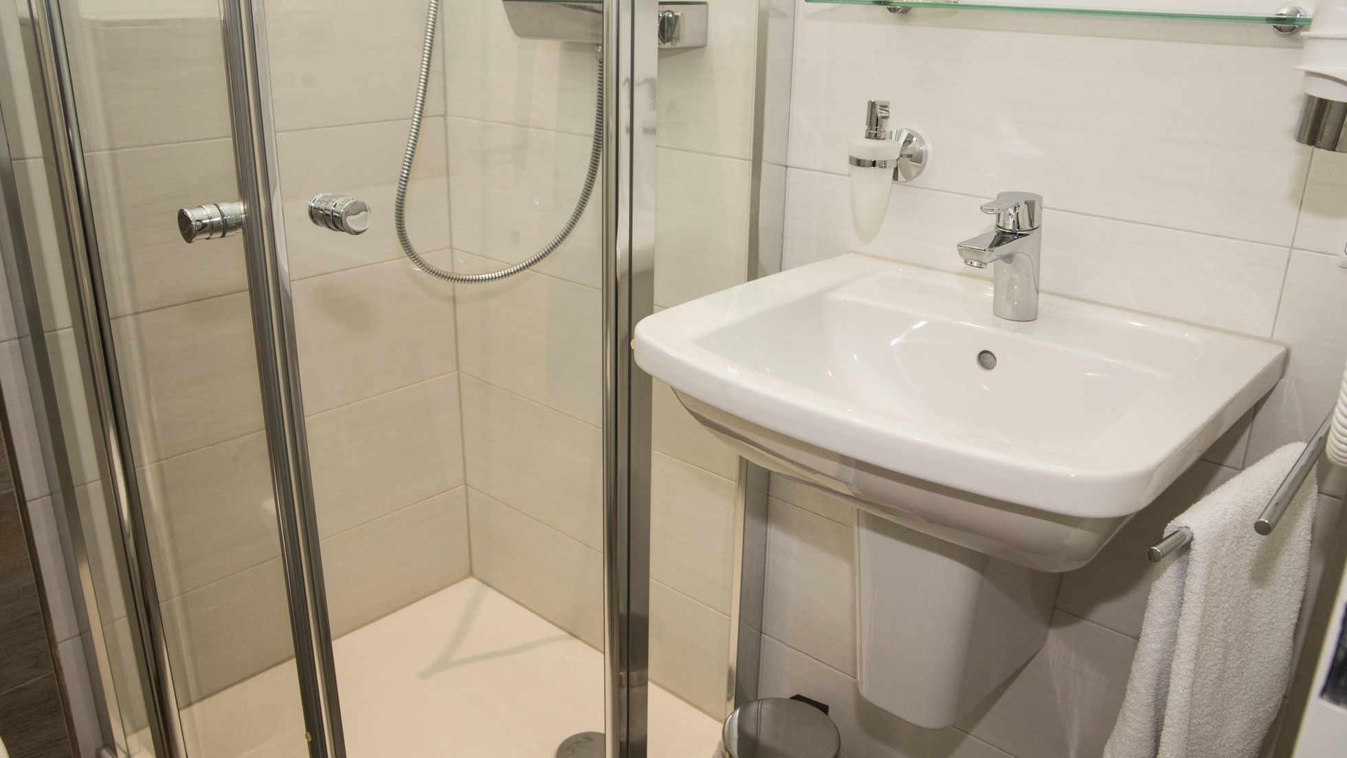 A modern bathroom with a glass-enclosed shower, a white sink, and a glass shelf above the sink.