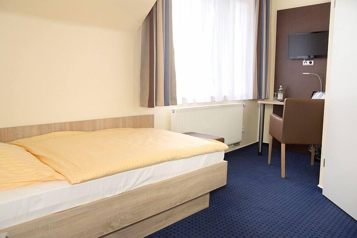 Une chambre d’hôtel équipée d’un lit, d’un bureau, d’une chaise, d’une télévision et d’une fenêtre avec des rideaux.