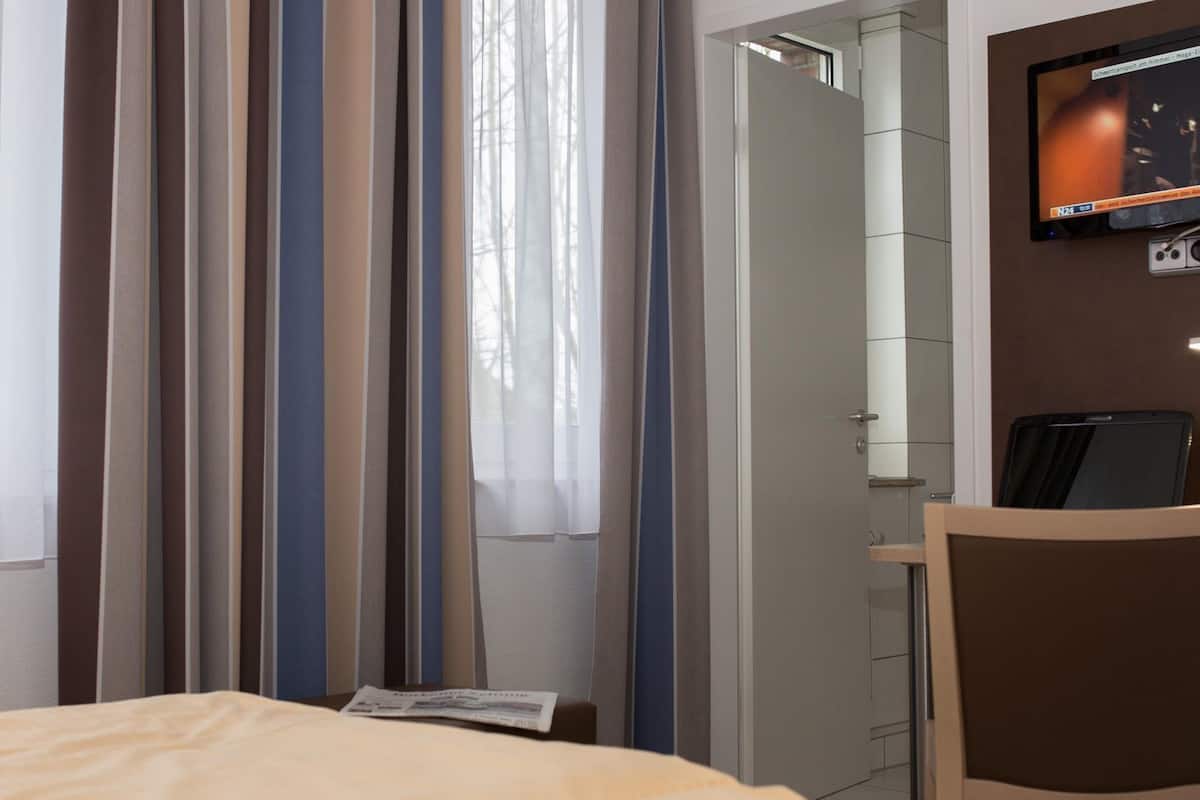 Une chambre d’hôtel avec un lit, un bureau et une chaise, une télévision et des rideaux.