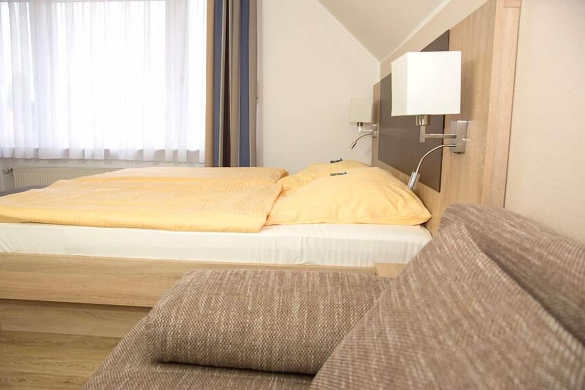 Une chambre d’hôtel avec un lit, une table de chevet avec une lampe et une fenêtre avec des rideaux.