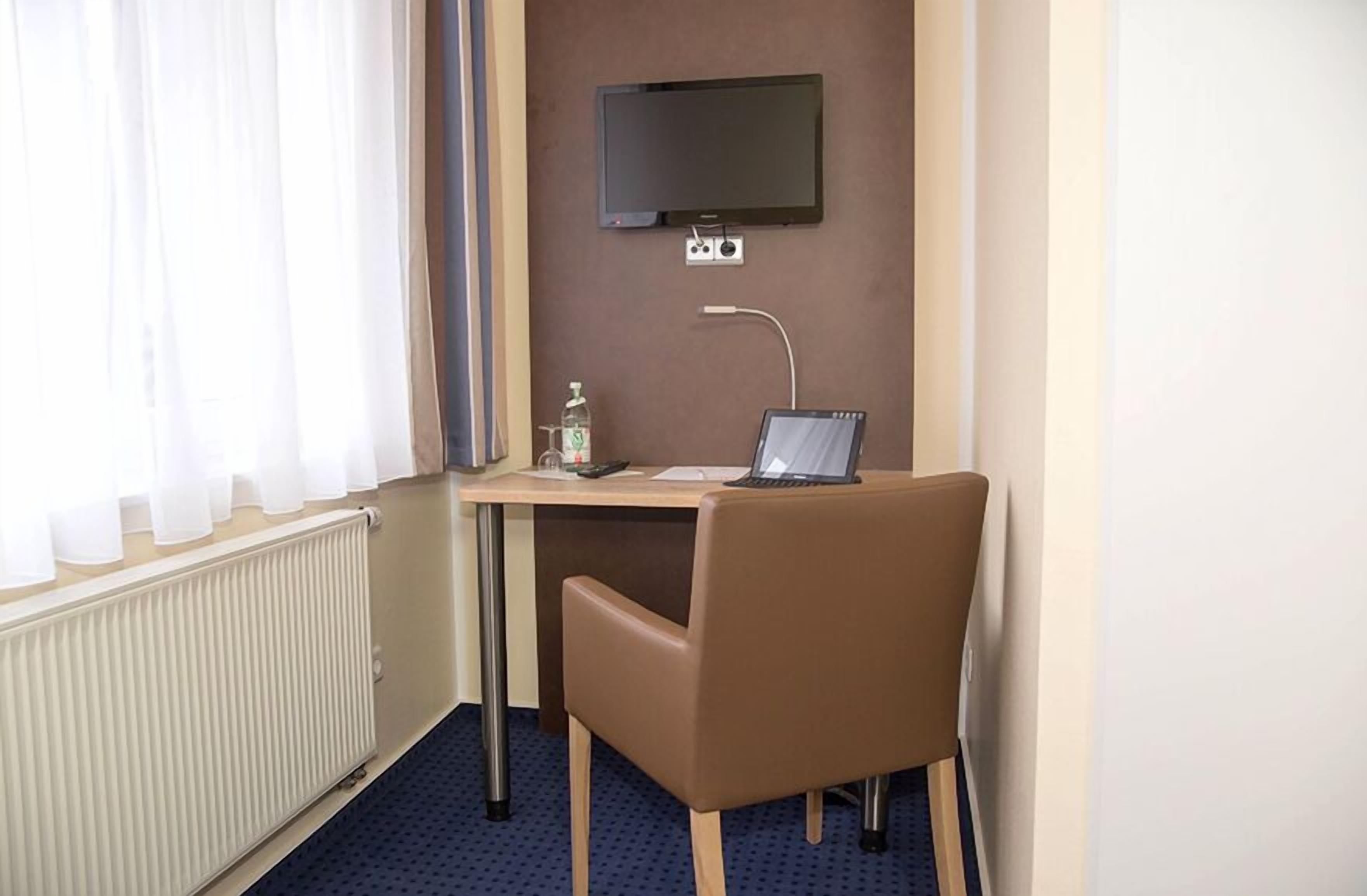 Habitación de hotel con escritorio, silla, ordenador portátil, televisor y botella de agua.