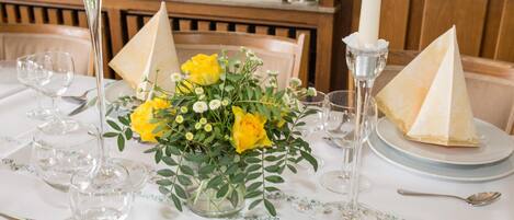 Una mesa dispuesta para una ocasión formal de cena, con un centro de flores amarillas, copas de cristal transparentes y porta servilletas en forma de pirámide.