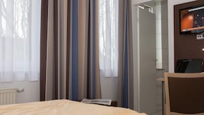 Hotellihuone, jossa on sänky, työpöytä, tuoli, televisio ja verhot.