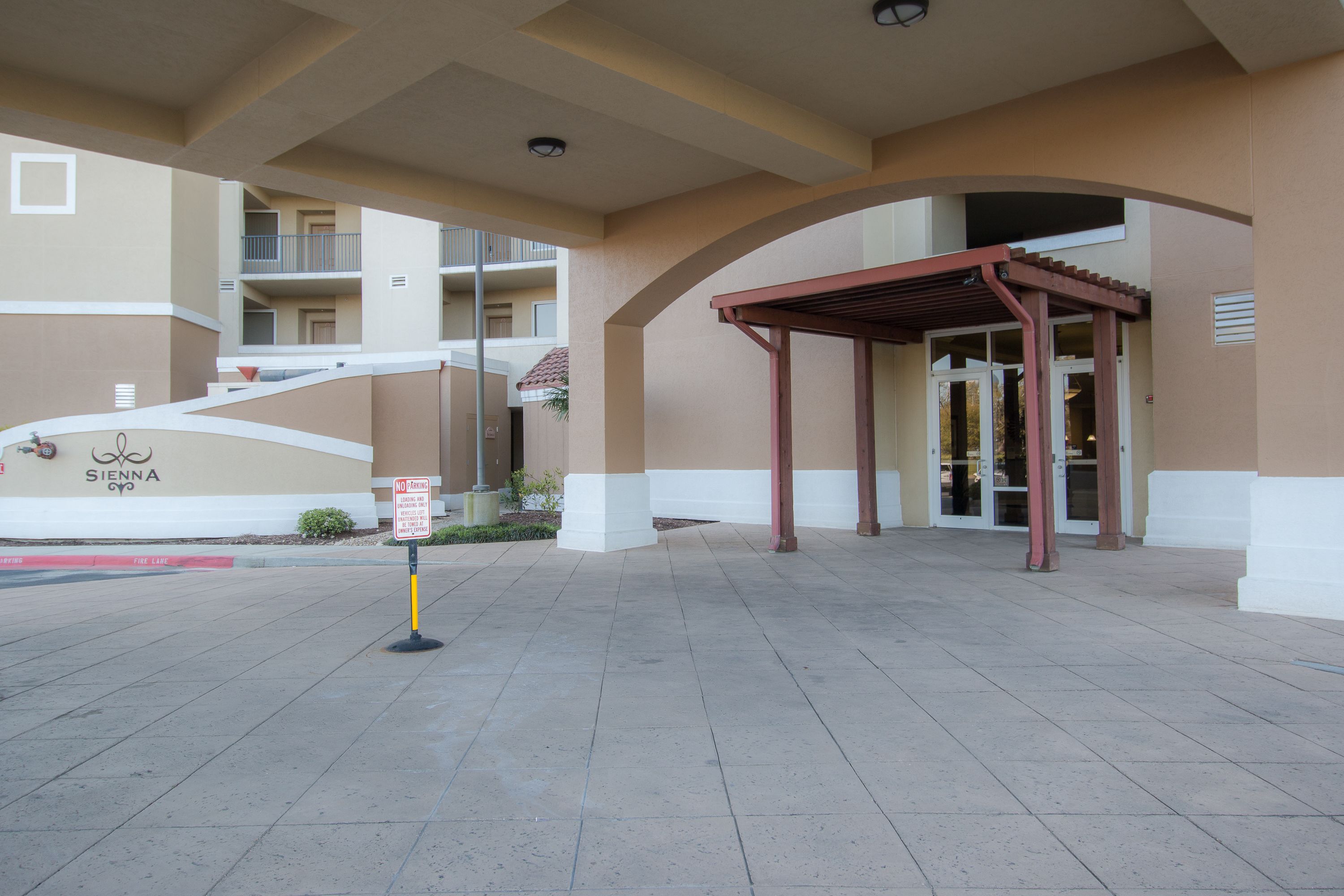 A hotel entrance with a covered walkway, a sign indicating a no-parking zone, and a visible balcony on the building.