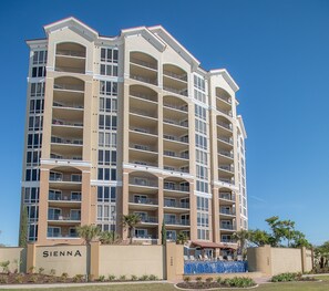 A multi-story hotel with balconies, a swimming pool, and a clear sky. - Sienna-Sienna 904 (Gulfport)