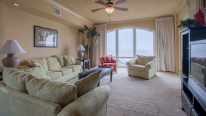 Un salon avec des canapés de couleur beige, une table basse, un téléviseur et un ventilateur de plafond.