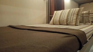A bed with a striped pillow and a brown blanket in a room with a wooden headboard and a light fixture above. - Pondok Backpacker City Square (Malang)