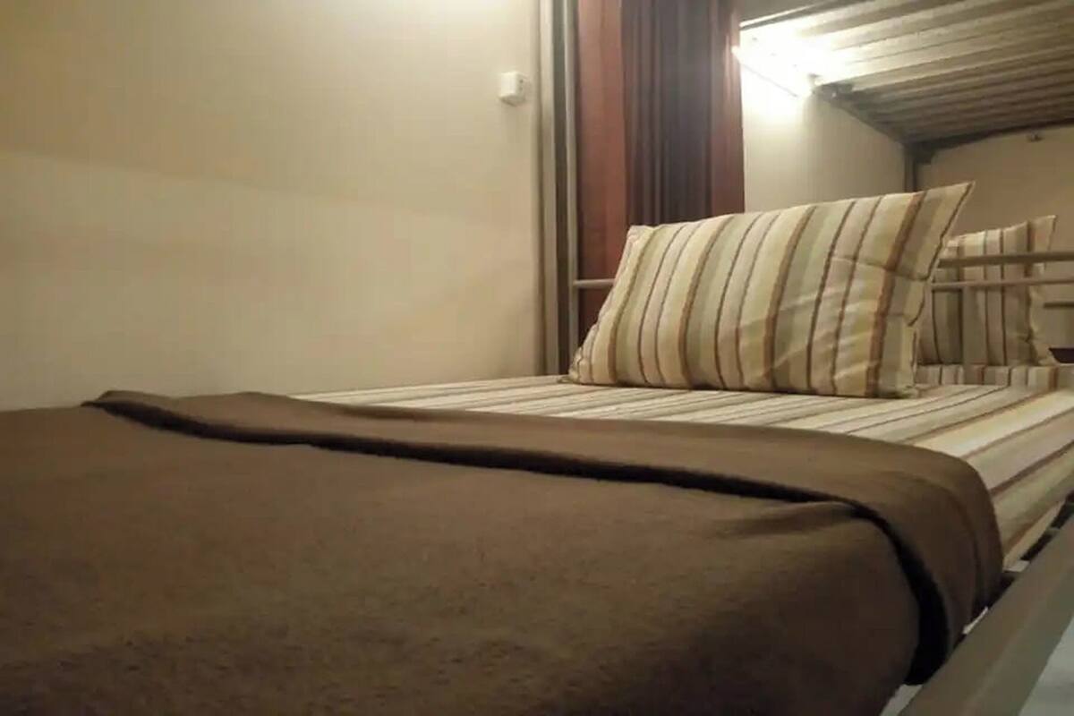 A bed with a striped pillow and a brown blanket in a room with a wooden headboard and a light fixture above.