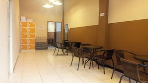 A hallway with tables and chairs, a storage unit with orange boxes, and a door leading to another room. - Pondok Backpacker City Square (Malang)