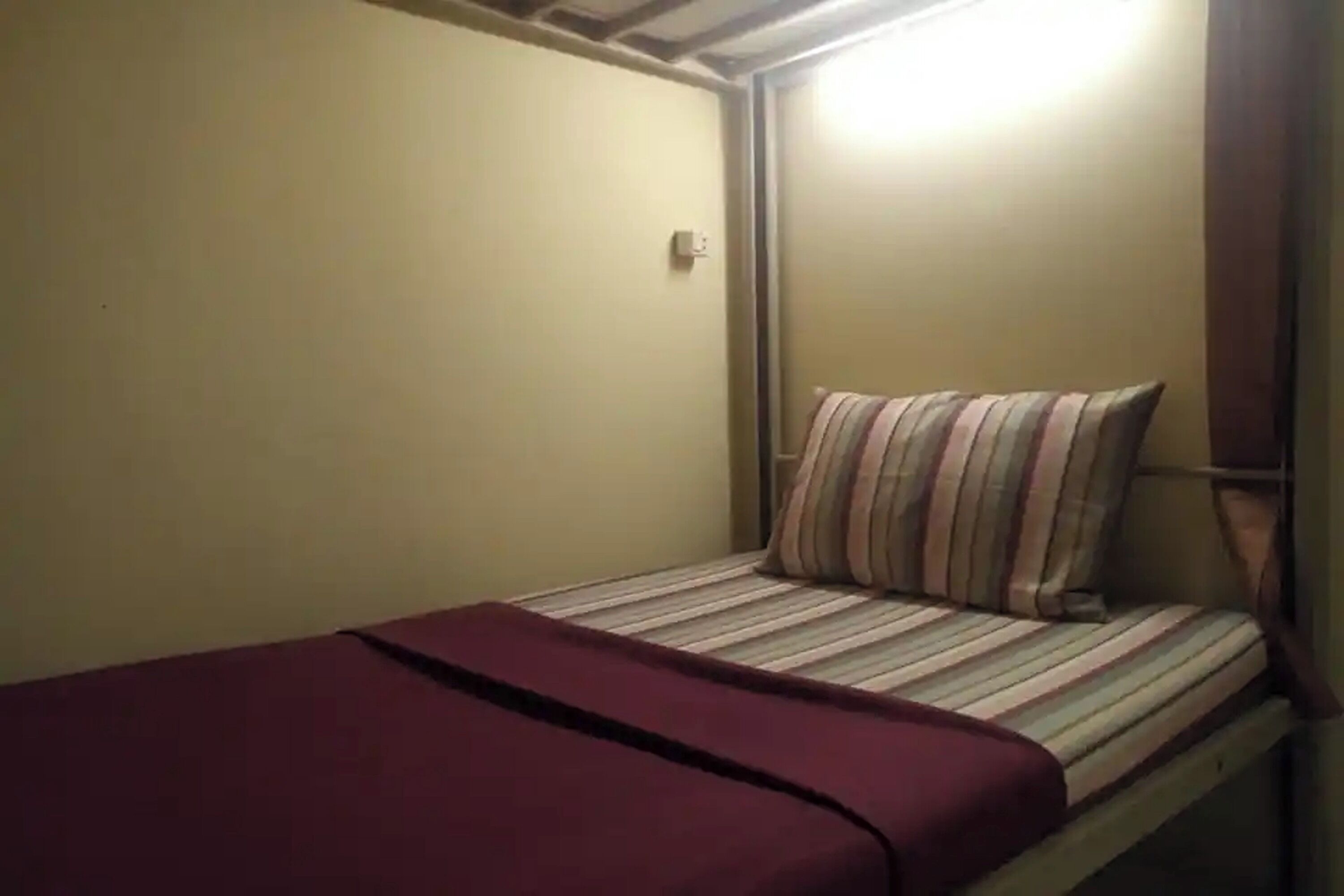 A small, single-bed room with a striped pillow and a maroon bedspread.