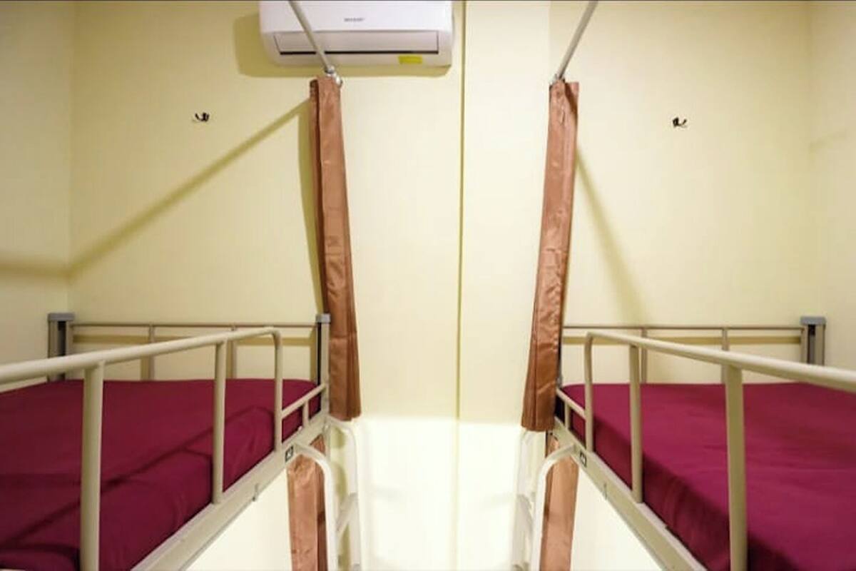 A hospital room with two beds, each with a metal frame and red bedding.