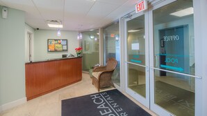 A reception area with a wooden desk, a wicker chair, and a glass door with a sign.