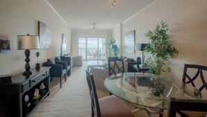 A spacious living room with a glass coffee table, black sofas, and a dining area with a glass table and chairs. - Sea Breeze-Sea Breeze 402 Deluxe (Biloxi)