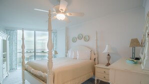 A four-poster bed with a ceiling fan, a bedside table with a lamp, and a dresser with a mirror. - Sea Breeze-Sea Breeze 410 Deluxe (Biloxi)