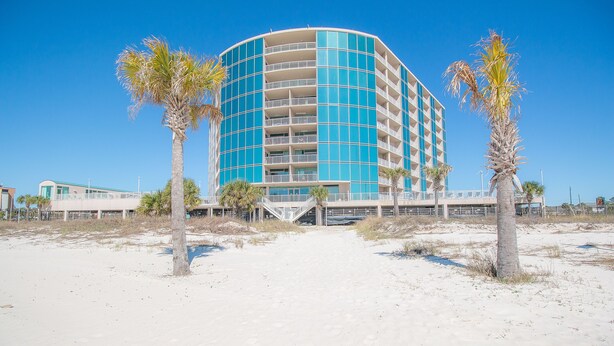 Un hotel frente a la playa con fachada curva, varios balcones y palmeras en primer plano.