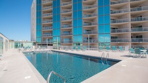 A swimming pool with a clear blue water, surrounded by a building with multiple balconies and a tiled deck. - Sea Breeze-Sea Breeze 607 (Biloxi)