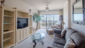 Uma sala de estar com televisão, sofá e mesa de centro de vidro.