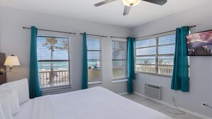 A hotel room with a bed, a ceiling fan, a window with a view of the beach, and a painting on the wall. - Paradise Oceanfront HBH (Hollywood)