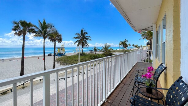 A balcony with a view of the beach, palm trees, and a lifeguard tower. - Paradise Oceanfront HBH (Hollywood)