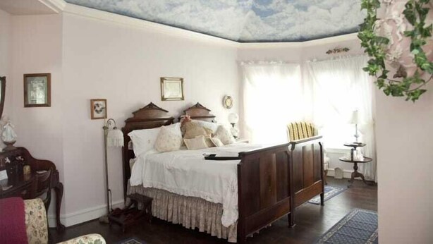 A bedroom with a bed, a ceiling fan, a window with curtains, and a wall-mounted plant. - Lillian Farms Bed & Breakfast (Washington)