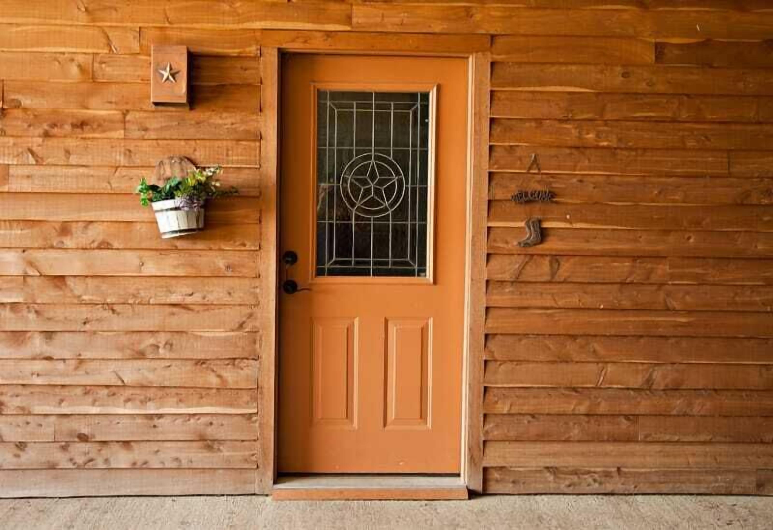 A wooden door with a metal grid window, a star-shaped decoration, and a small plant on the wall.