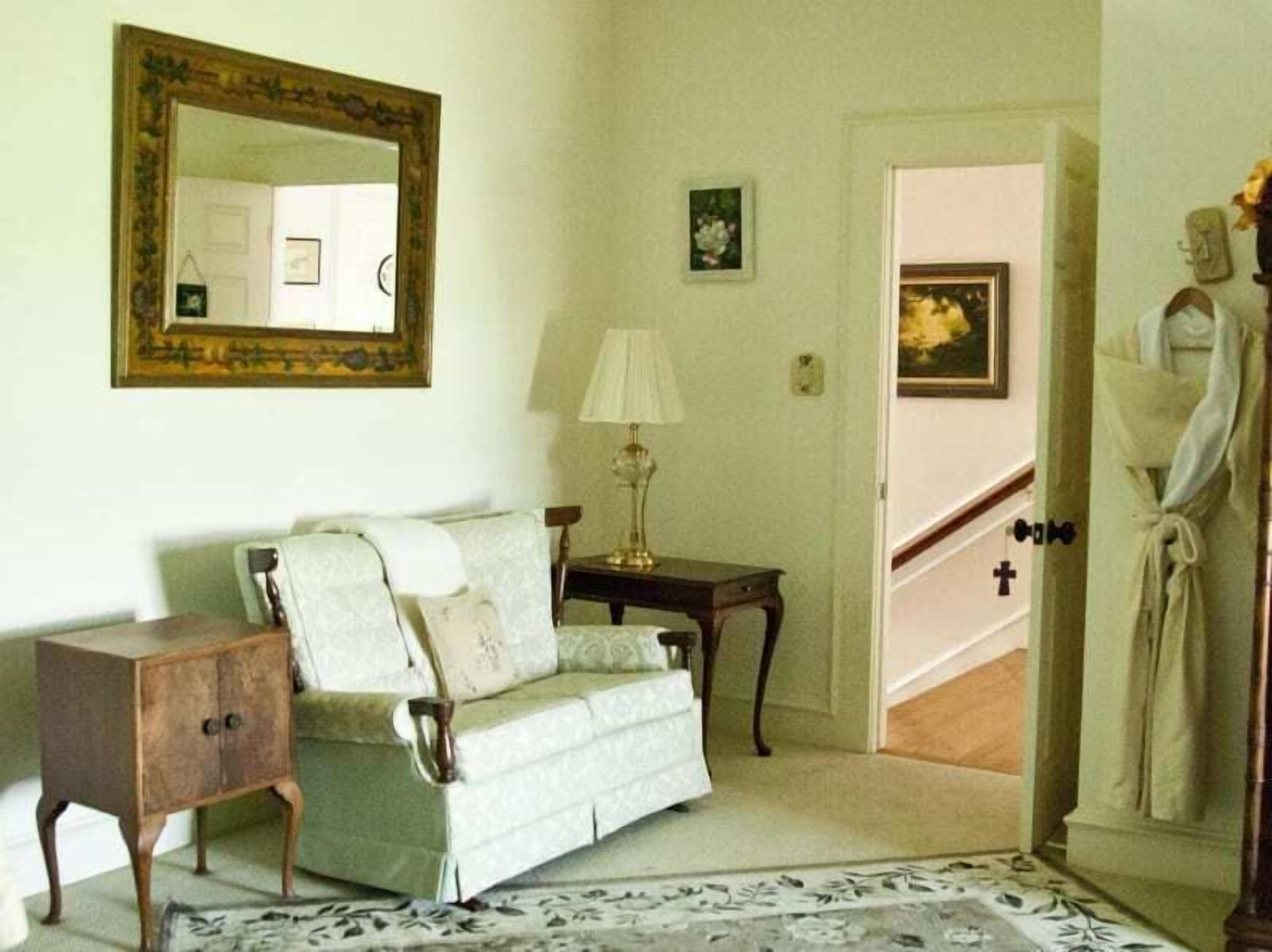 A room with a sofa, a small table, a lamp, a mirror, and a statue.