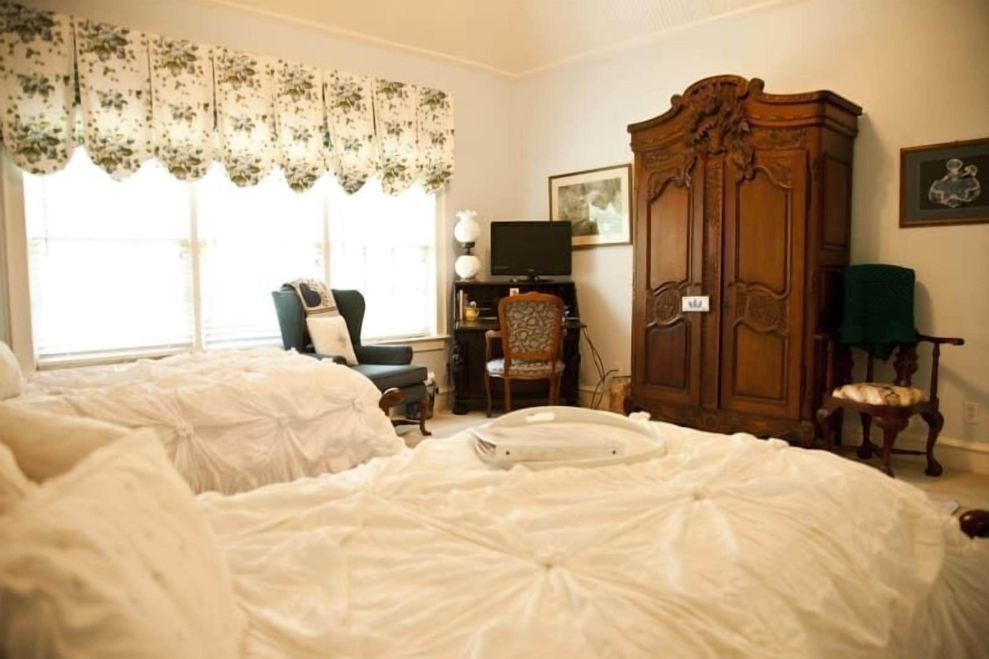 A bedroom with a large bed, a wooden wardrobe, a television, and a chair.