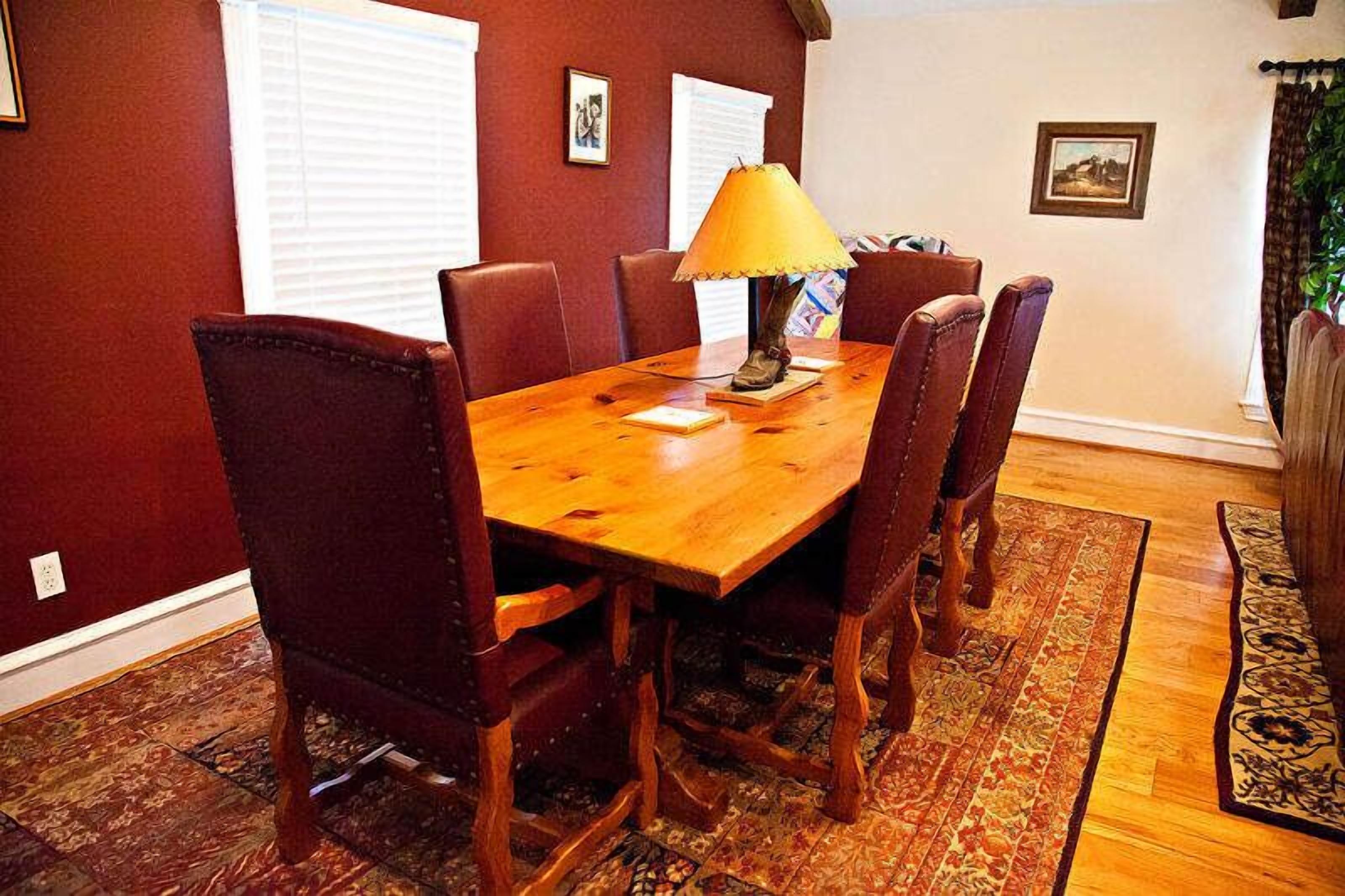 A wooden dining table with six chairs, a lamp, and a patterned rug.