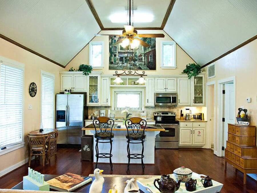 A spacious kitchen with white cabinetry, a central island with bar stools, a chandelier, and a large window.