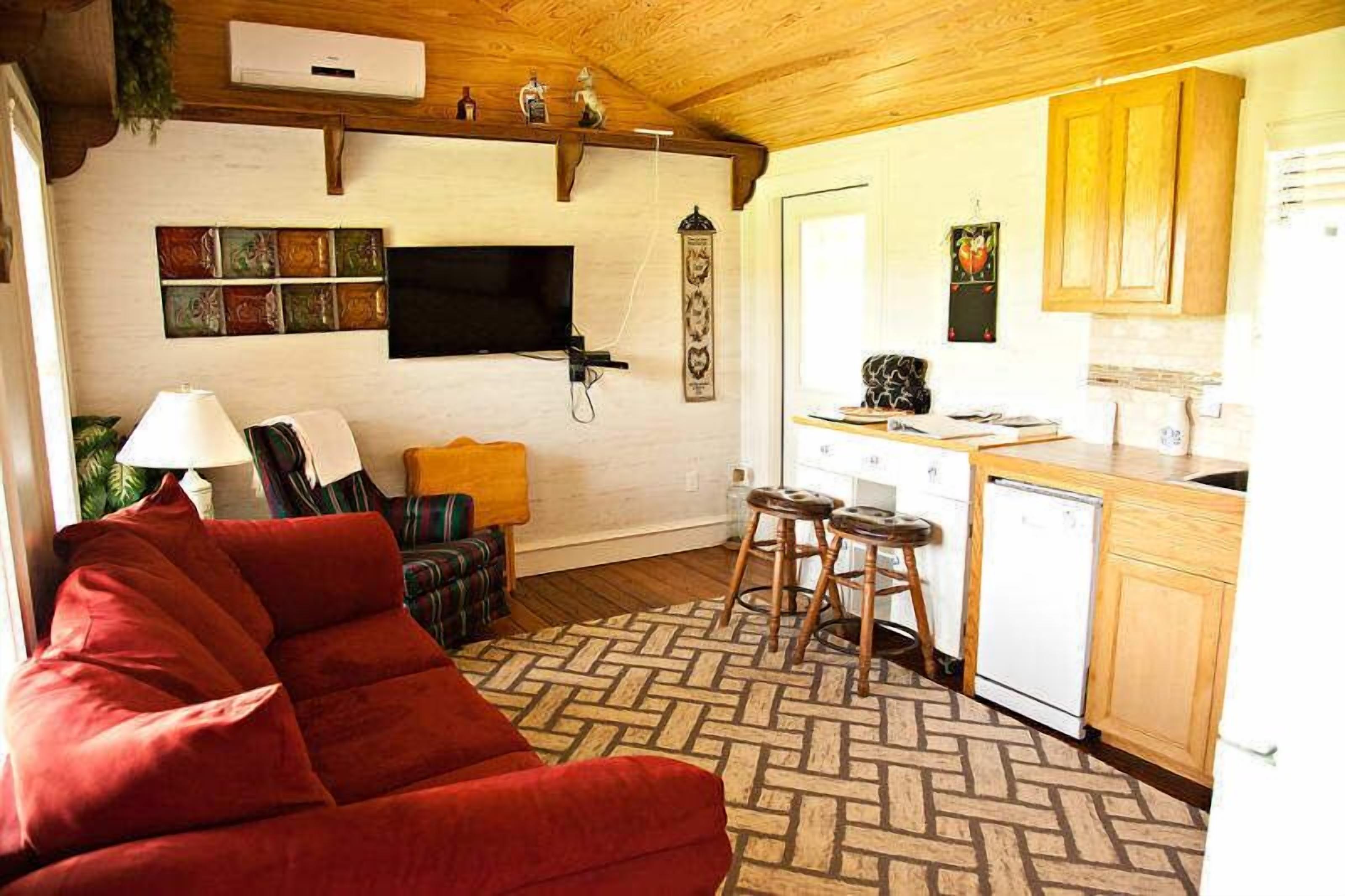 A living room with a red sofa, a TV, and a kitchen area with wooden cabinets and a dishwasher.
