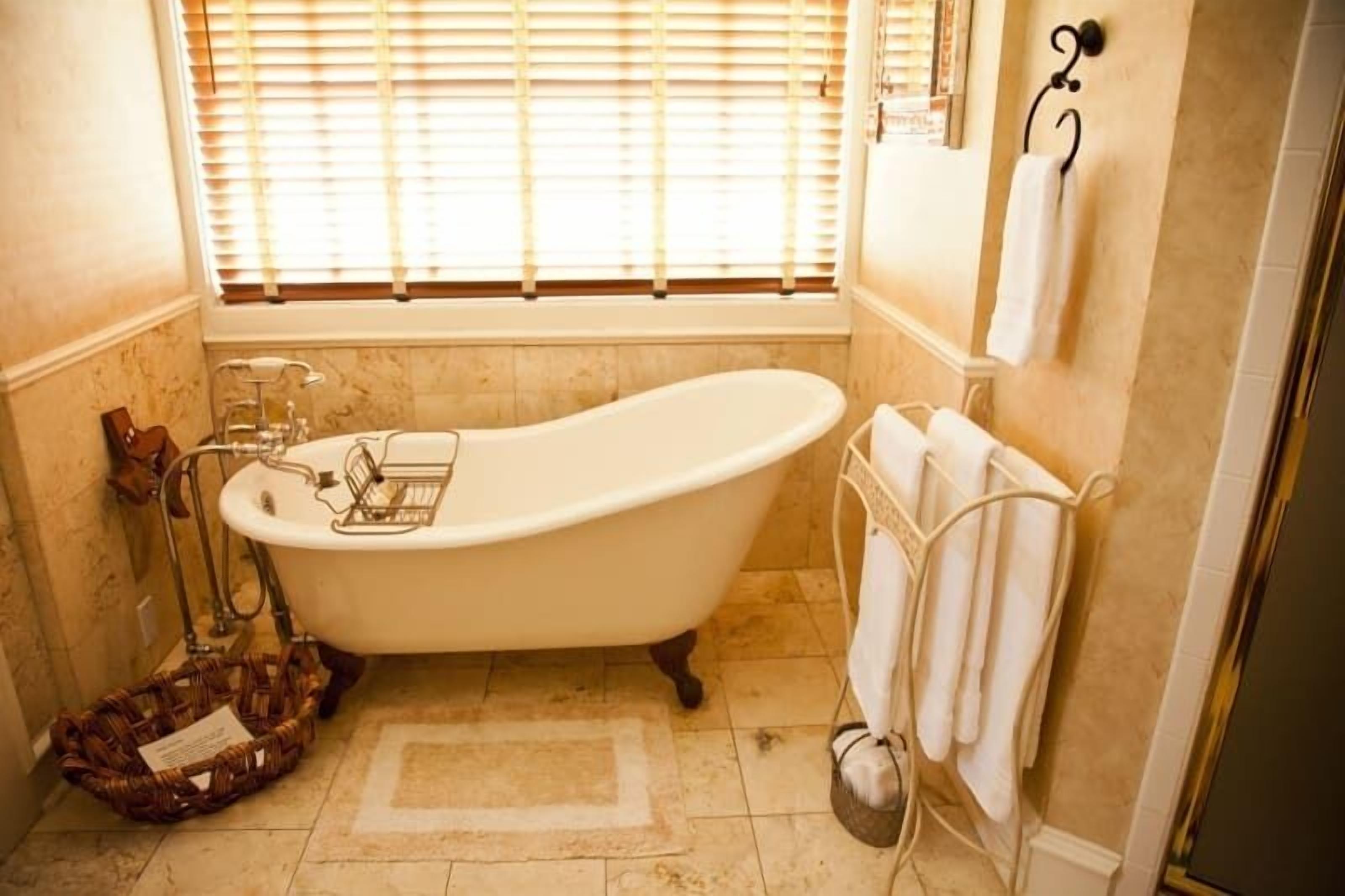 Ein Badezimmer mit einer Badewanne auf Füßen, einem Fenster mit Jalousien, einem Handtuchhalter und einem Korbwannen.