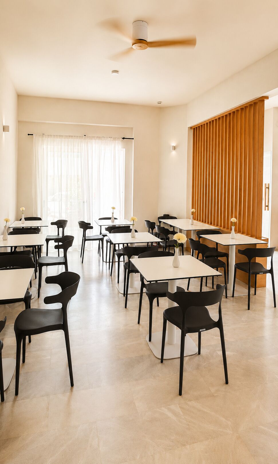 A spacious room with multiple tables and chairs, a ceiling fan, and a large window with curtains.