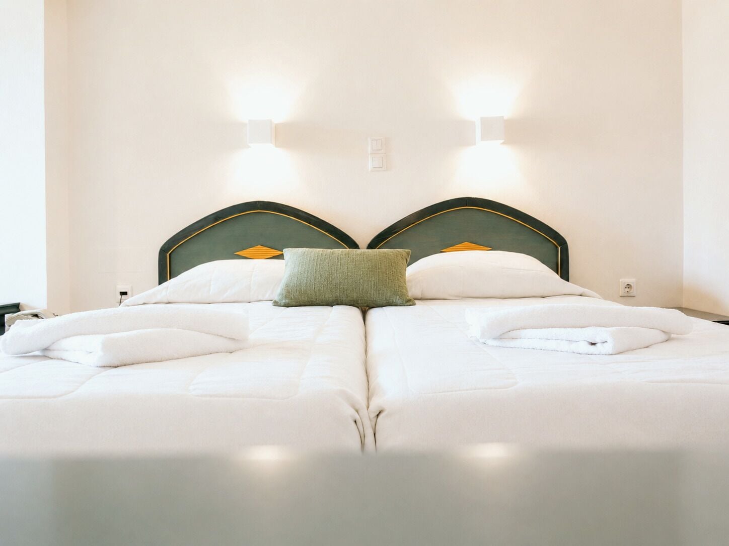 Ein Doppelbett mit grünem Kopfteil, zwei Wandleuchten und einem grünen Kopfkissen.