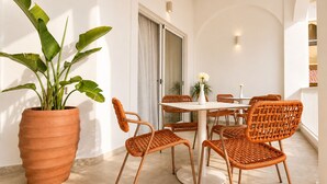 Comedor con una mesa redonda, sillas de mimbre, una planta en maceta y un ventanal corredizo.