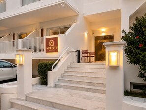 A hotel entrance with a marble staircase, a sign reading 'MELITTI LUXURY,' and outdoor seating. - Melitti Lucent (Rethymno)