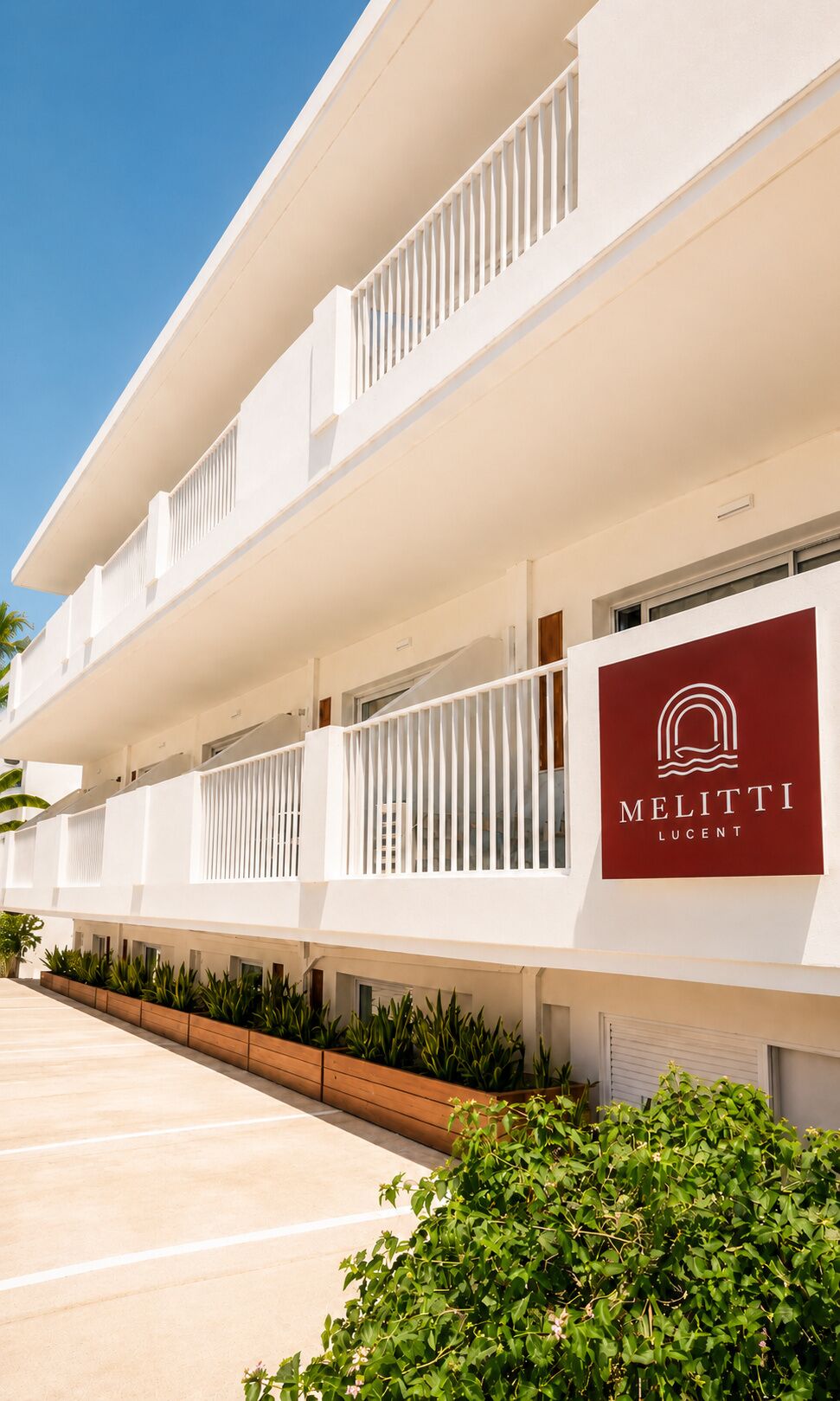 A multi-story hotel with balconies, a parking area, and a sign for 'MELITTI LUCENT'.