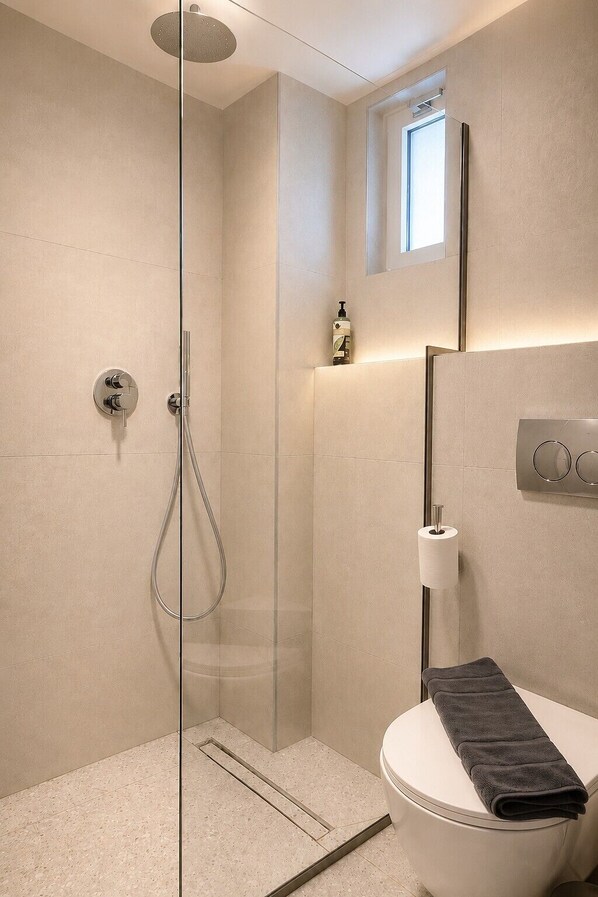 A modern bathroom with a glass-enclosed shower, a toilet, and a small window above the sink.