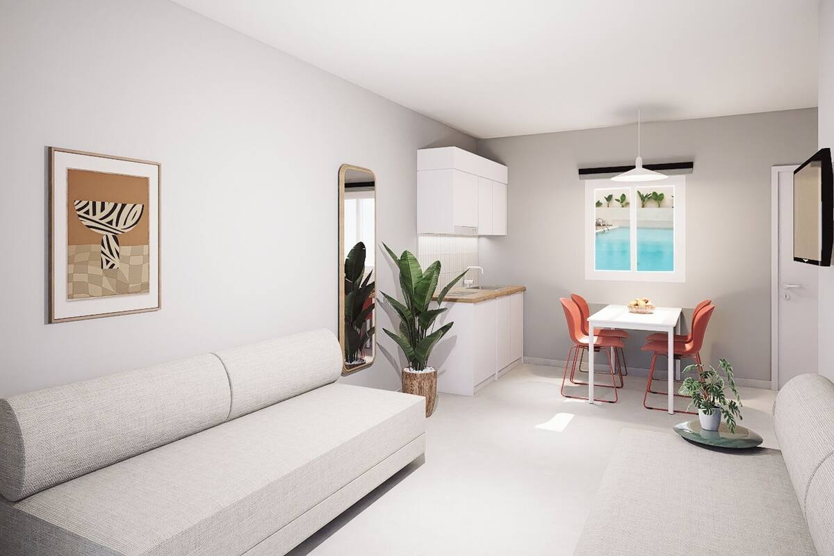 A modern living room with a sofa, a dining table with chairs, a kitchen area, and a view of a pool.