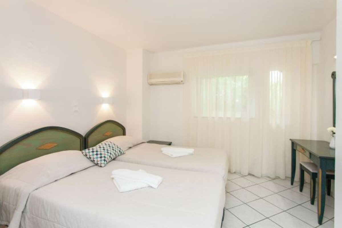 A hotel room with two beds, a desk, and an air conditioning unit.